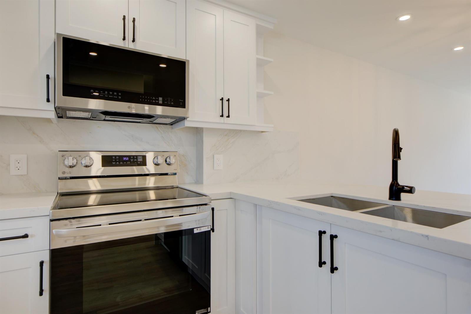 A modern kitchen features white cabinets, stainless steel appliances, and a marble-style backsplash — 201 N Ocean Boulevard # 207, Pompano Beach FL 33062, POMPANO BEACH, FL