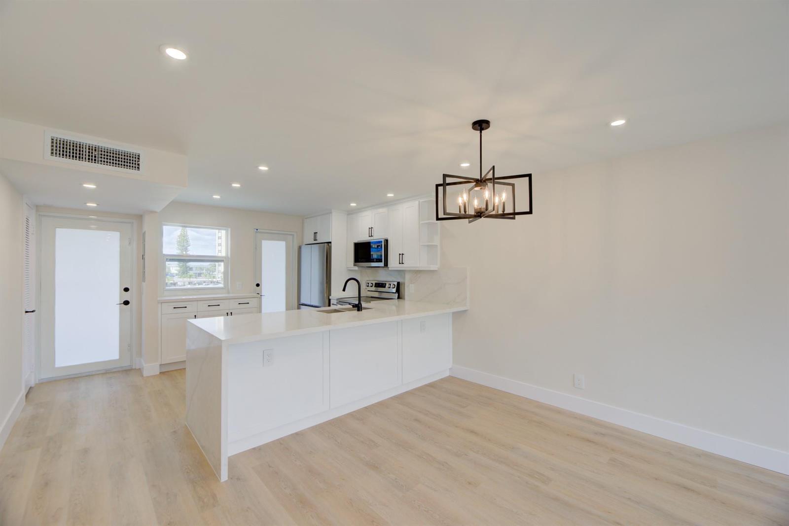 A modern kitchen features white cabinetry, a quartz island, and a black metal chandelier — 201 N Ocean Boulevard # 207, Pompano Beach FL 33062, POMPANO BEACH, FL