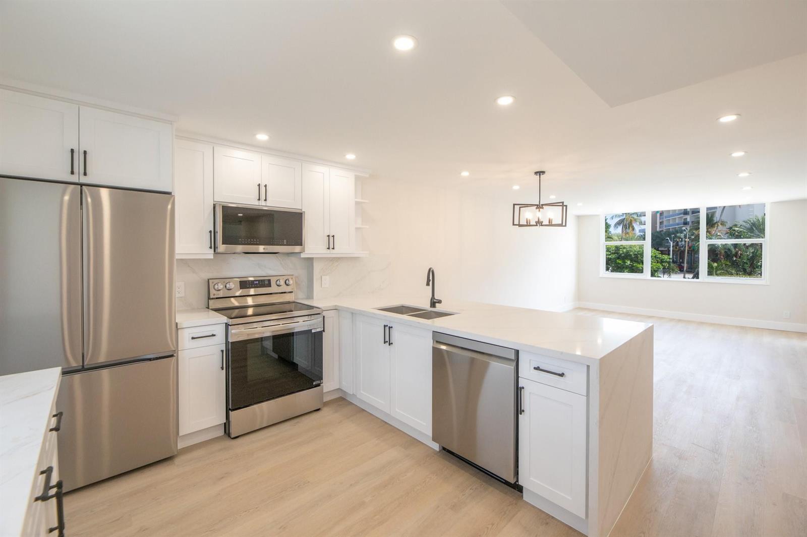 A modern kitchen features white cabinets, stainless steel appliances, and a quartz-topped island — 201 N Ocean Boulevard # 207, Pompano Beach FL 33062, POMPANO BEACH, FL