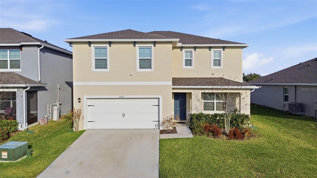 A two-story house with a beige stucco exterior, a white garage door, and a driveway — 2029 APALACHICOLA LANE, SANFORD, FL