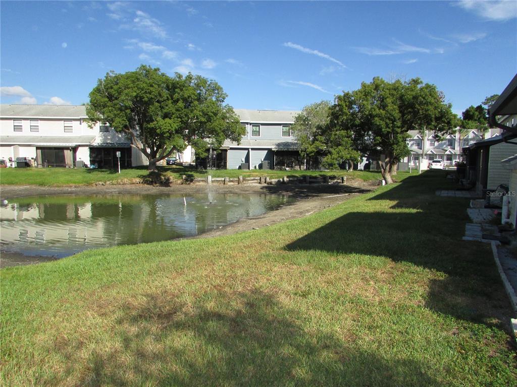 A small pond with a fountain sits in front of multi-story residential townhomes — 12715 RAEBURN WAY, TAMPA, FL