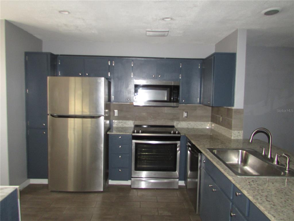 A kitchen features blue cabinets, stainless steel appliances, and granite countertops — 12715 RAEBURN WAY, TAMPA, FL