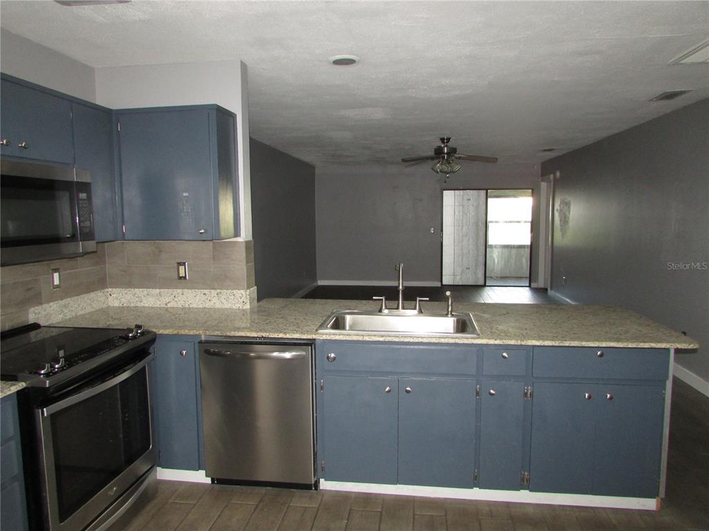 A kitchen with blue cabinets, stainless steel appliances, and granite countertops overlooks a living area — 12715 RAEBURN WAY, TAMPA, FL