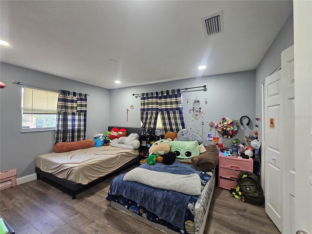 A bedroom features two twin beds, gray walls, wood-look flooring, and plaid curtains — 3110 22ND AVENUE W, BRADENTON, FL