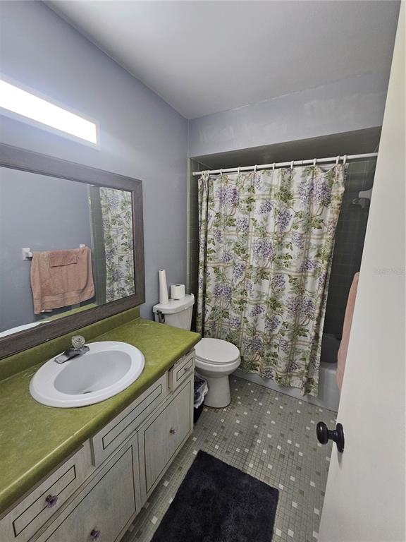 A bathroom features a green vanity countertop, a floral shower curtain, and tiled flooring — 3110 22ND AVENUE W, BRADENTON, FL