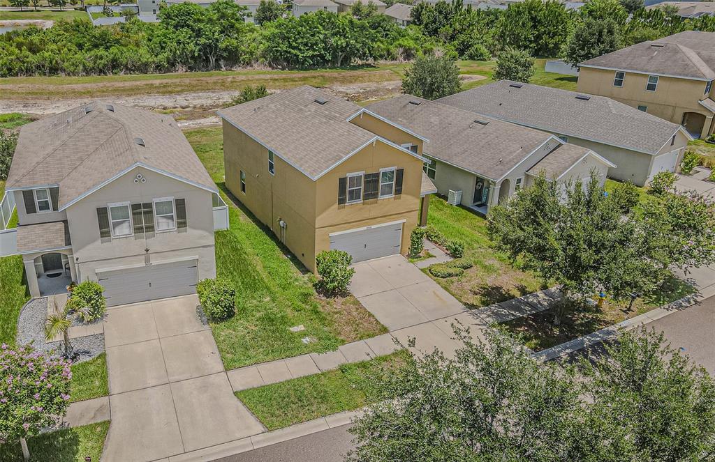 An aerial view shows three suburban houses with driveways and lawns in a residential neighborhood — 10536 WHISPERING HAMMOCK DRIVE, RIVERVIEW, FL