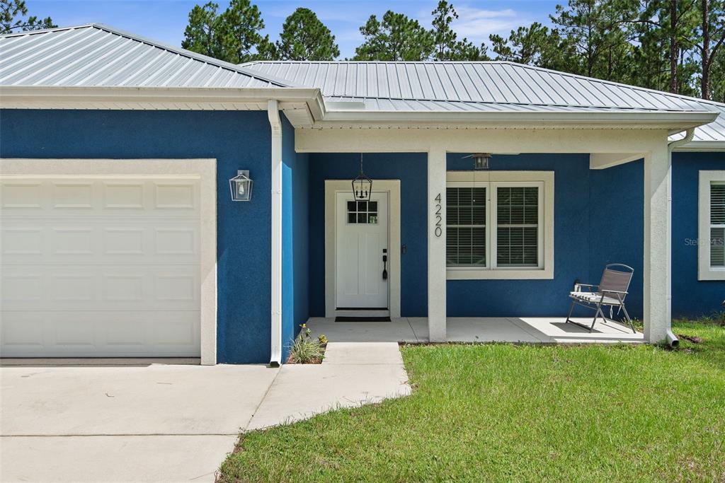 A blue house exterior features a white garage door, a front porch, and a walkway — 4220 PALATKA BOULEVARD, HASTINGS, FL