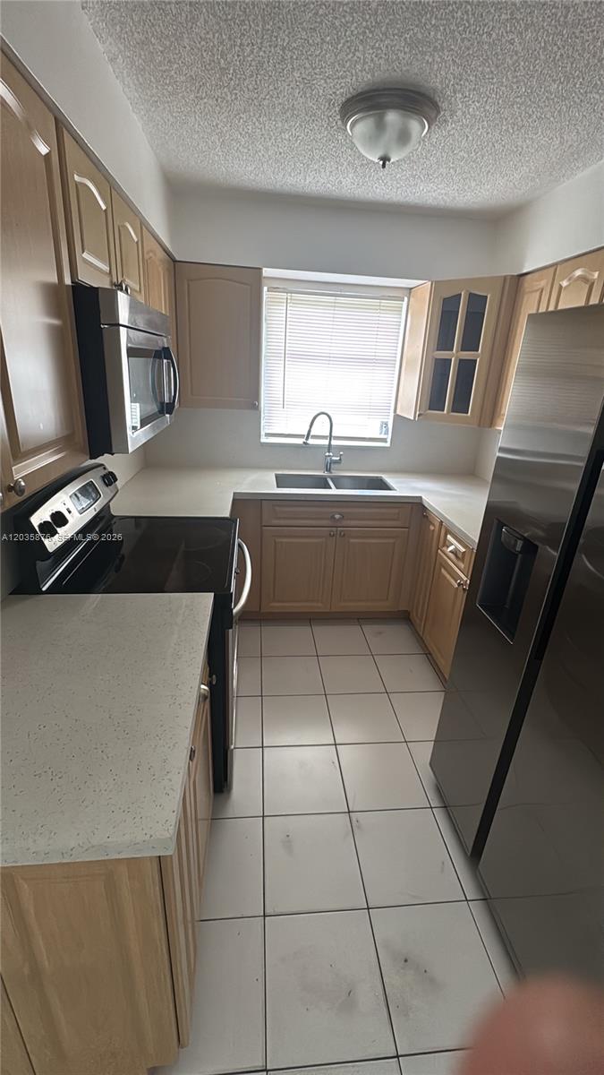 A kitchen features light wood cabinets, stainless steel appliances, white countertops, and tiled flooring — 830 W 75th St # 1, Hialeah FL 33014, HIALEAH, FL