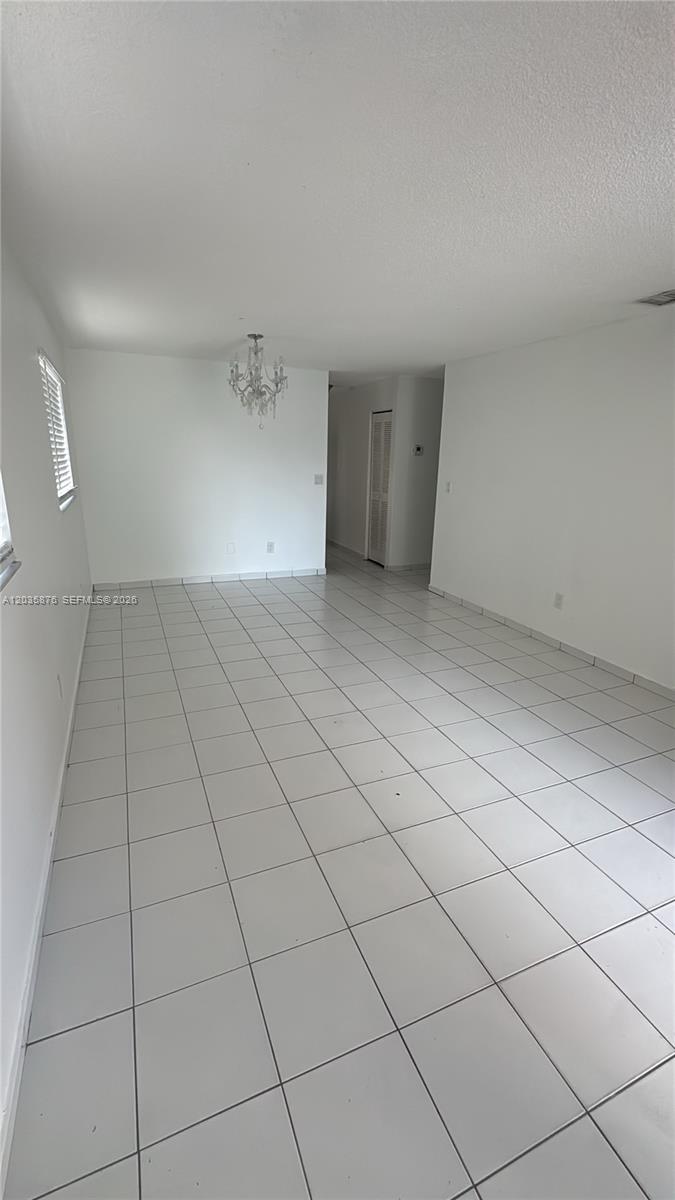 An empty room with white walls, white tile flooring, and a crystal chandelier — 830 W 75th St # 1, Hialeah FL 33014, HIALEAH, FL
