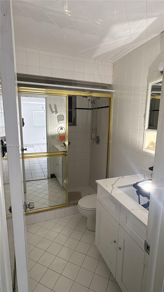 A bathroom features a white vanity, a tiled floor, and a shower with gold-framed doors — 830 W 75th St # 1, Hialeah FL 33014, HIALEAH, FL