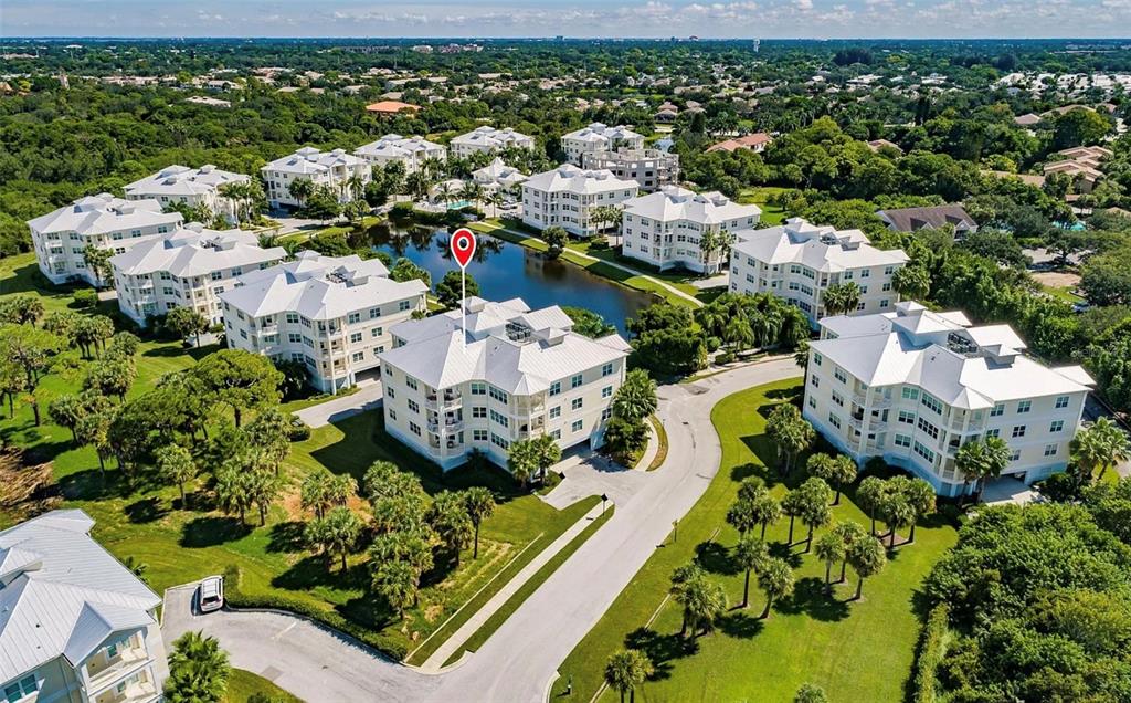 An aerial view shows multi-story residential buildings with white roofs surrounding a central pond — 7840 34TH AVENUE W UNIT 102, BRADENTON, FL