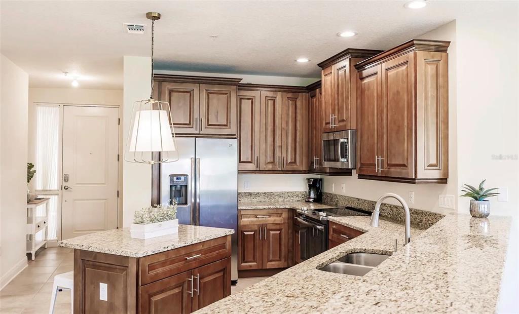 A kitchen with wood cabinets, granite countertops, a stainless steel refrigerator, and a center island — 7840 34TH AVENUE W UNIT 102, BRADENTON, FL