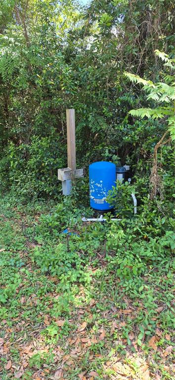 A blue water well pressure tank sits outdoors in a wooded area near a wooden post — 1491 SE 189TH AVENUE, SILVER SPRINGS, FL