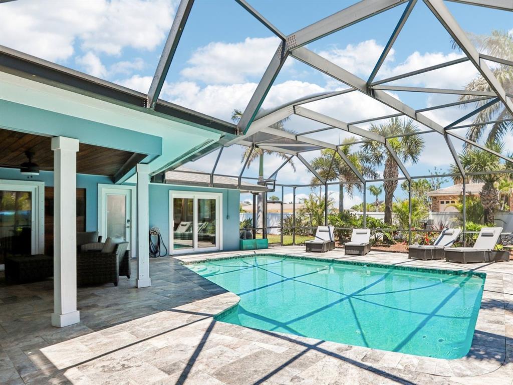 A screened-in swimming pool with a stone patio and a blue house exterior — 3203 HIBISCUS DRIVE W, BELLEAIR BEACH, FL