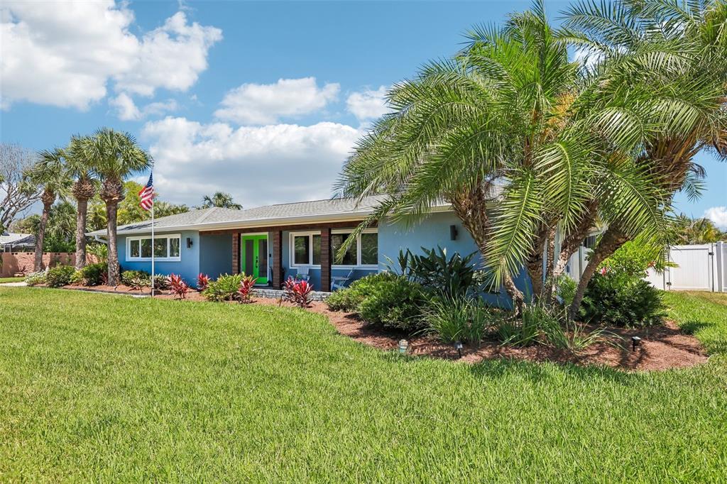 A light blue single-story house features a bright green front door and palm trees — 3203 HIBISCUS DRIVE W, BELLEAIR BEACH, FL