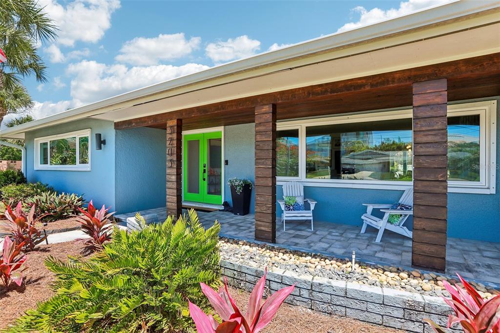A blue house exterior features a covered porch with dark wood columns and a green door — 3203 HIBISCUS DRIVE W, BELLEAIR BEACH, FL