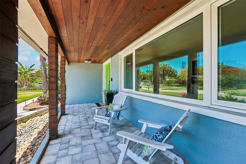 A covered front porch features a wood-paneled ceiling, blue stucco walls, and two white chairs — 3203 HIBISCUS DRIVE W, BELLEAIR BEACH, FL