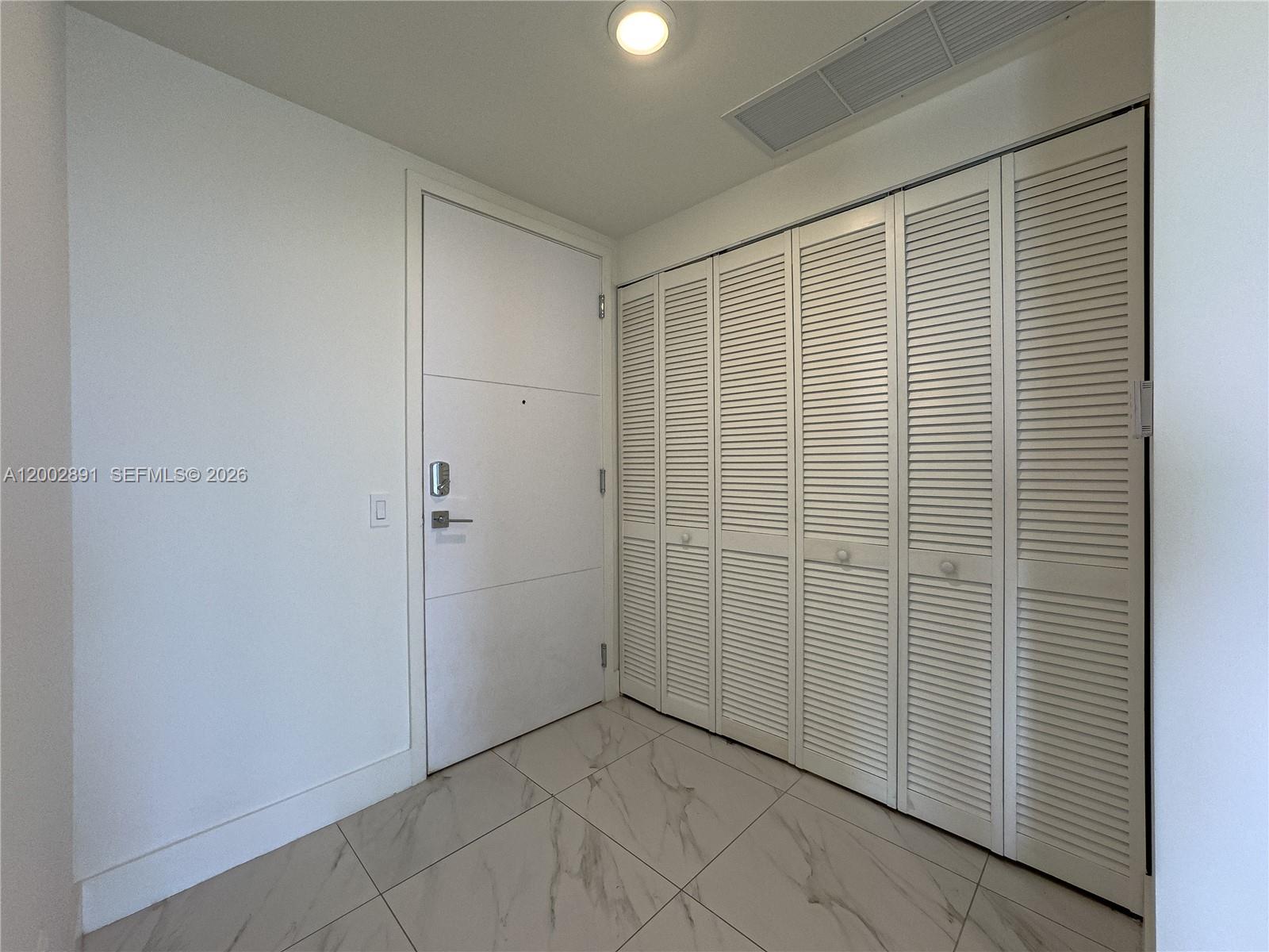 An entryway features a white door, louvered closet doors, and light-colored marble-patterned tile flooring — 2000 Metropica Way # 2009, Sunrise FL 33323, SUNRISE, FL