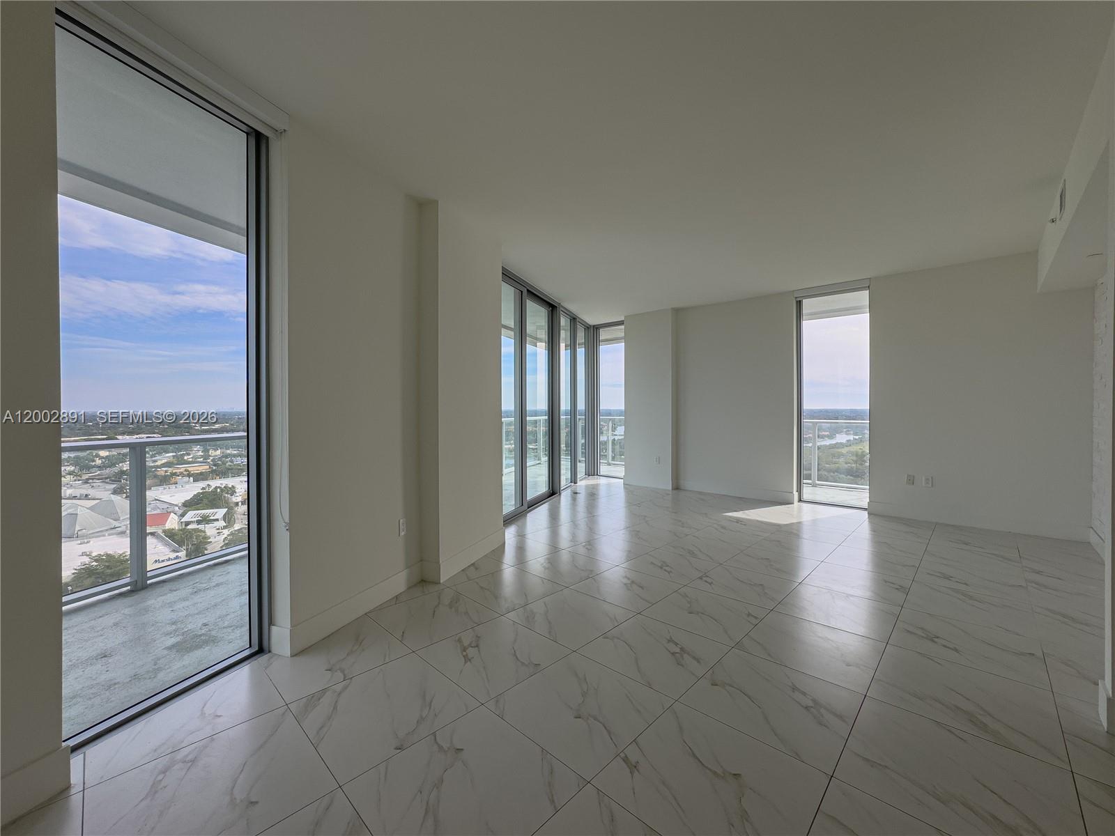 An empty room features white marble-look tile floors, floor-to-ceiling windows, and a balcony view — 2000 Metropica Way # 2009, Sunrise FL 33323, SUNRISE, FL