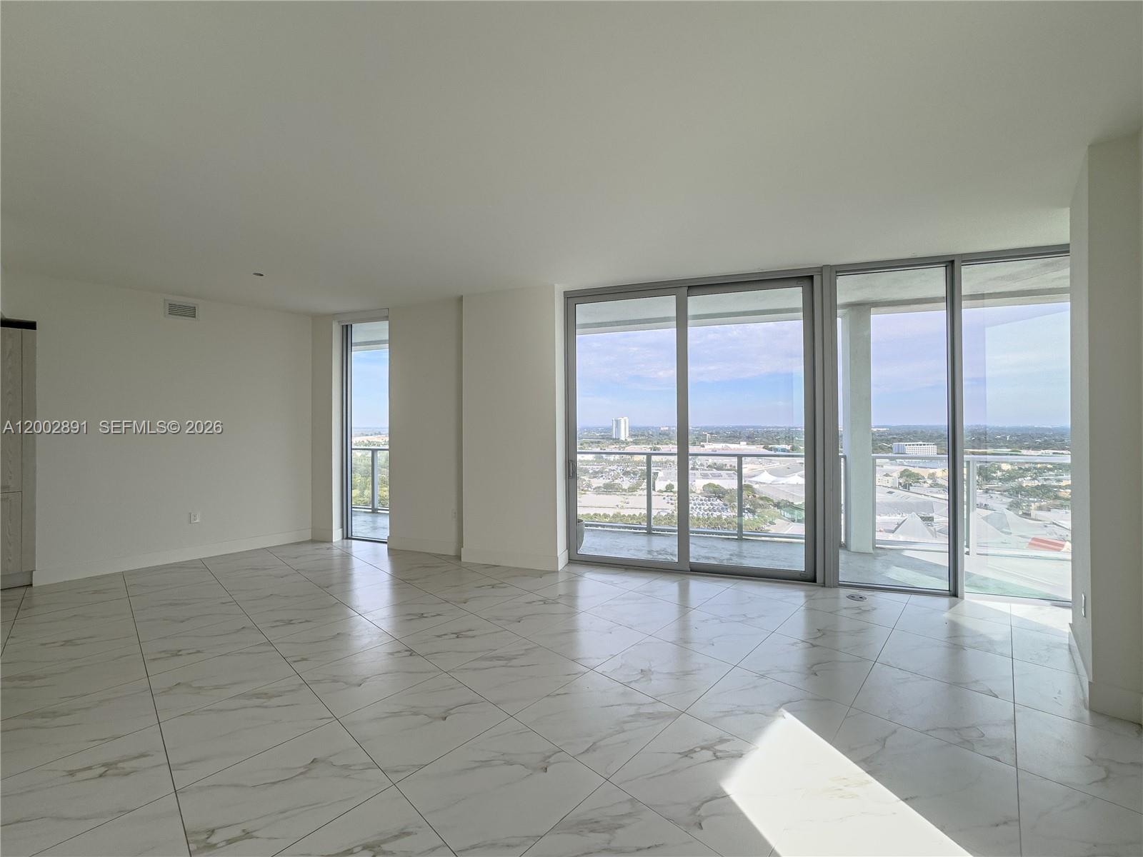 An empty room features white marble-look tile flooring, white walls, and large sliding glass doors — 2000 Metropica Way # 2009, Sunrise FL 33323, SUNRISE, FL