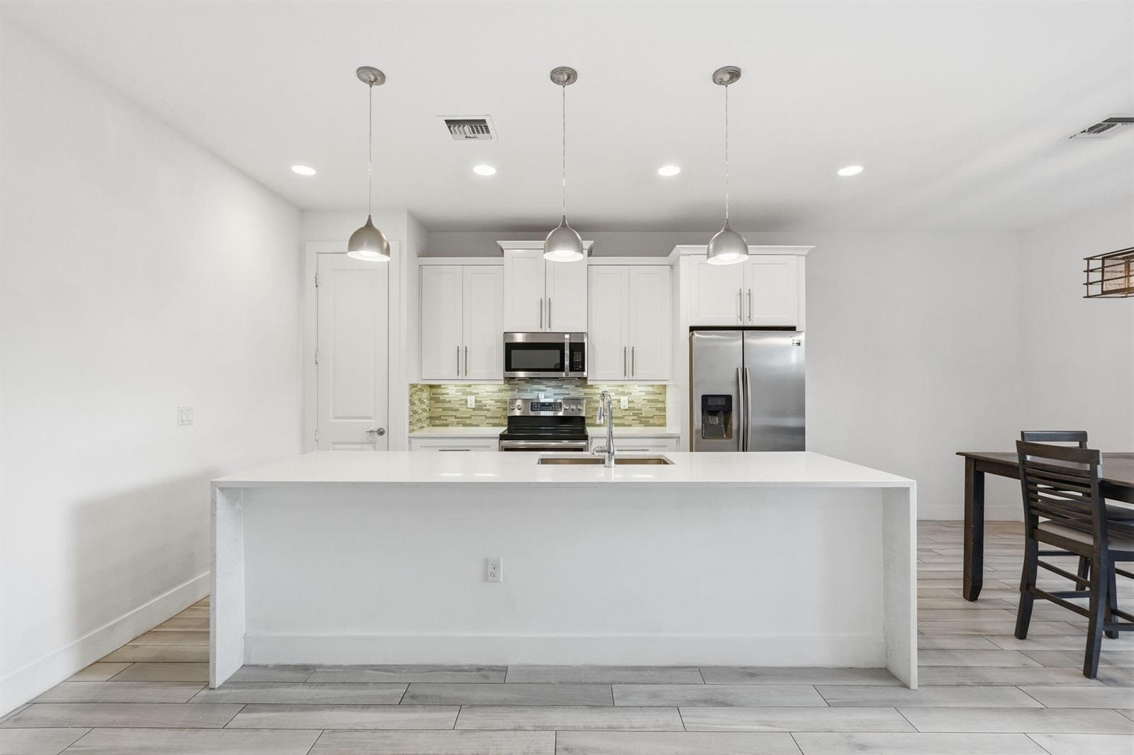 A modern kitchen features white cabinetry, stainless steel appliances, and a large central island — 3193 Santa Catalina Place, FL 33467, FL