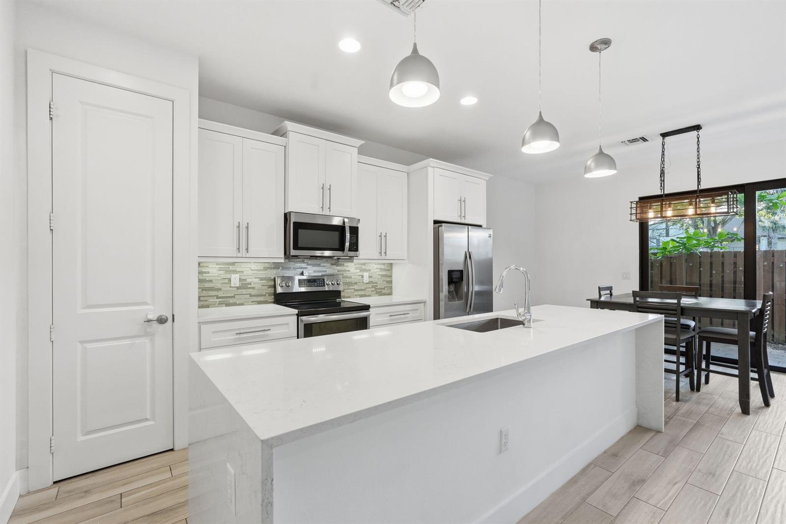 A modern kitchen features white cabinetry, a quartz island with a sink, and pendant lighting — 3193 Santa Catalina Place, FL 33467, FL