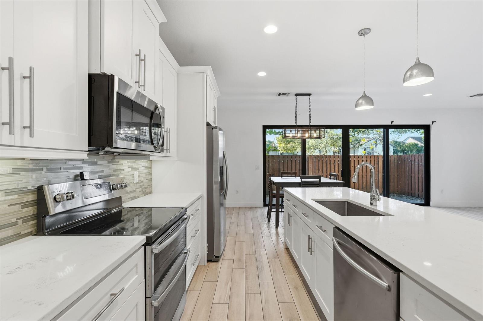 A modern kitchen features white cabinets, stainless steel appliances, a center island, and wood-look flooring — 3193 Santa Catalina Place, FL 33467, FL