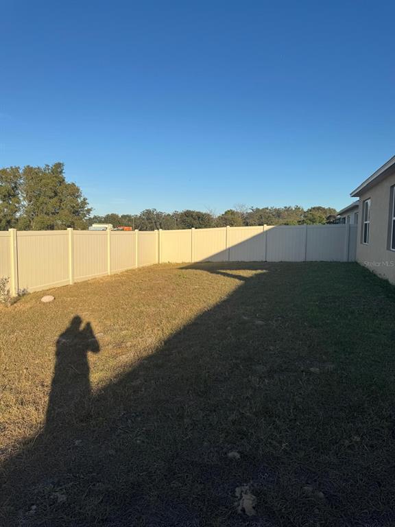A grassy backyard features a tan vinyl privacy fence and a portion of a house — 528 BOARDWALK AVENUE, HAINES CITY, FL