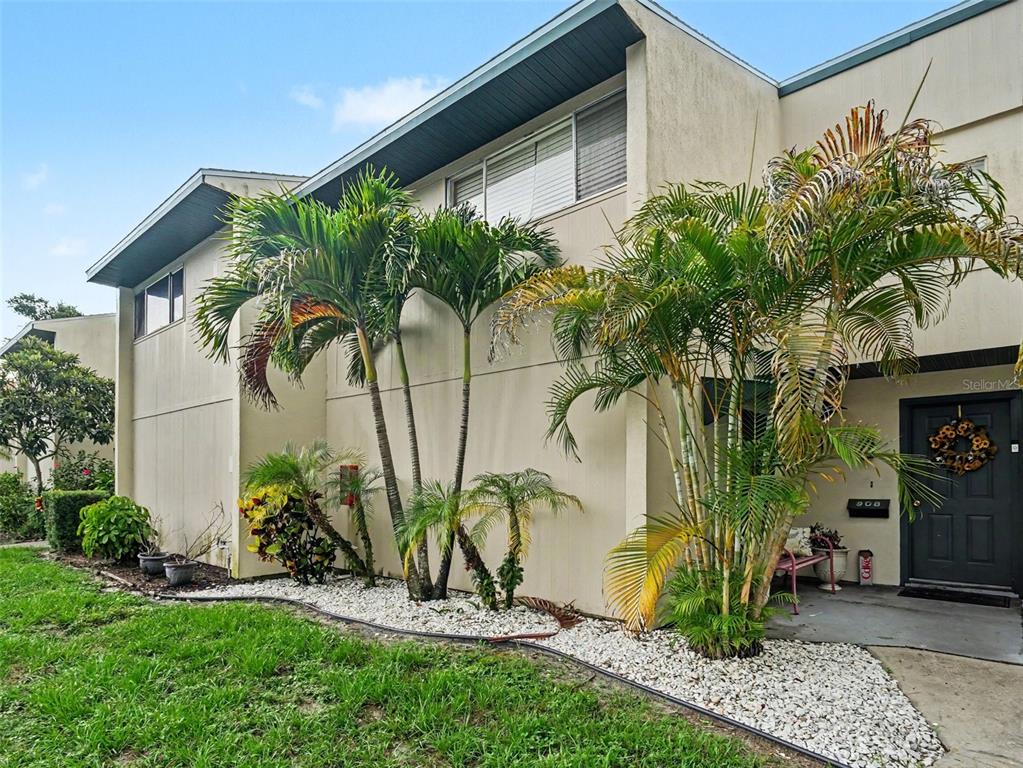 A two-story townhouse exterior features palm trees, a gravel garden bed, and a dark front door — 908 BYRON LANE UNIT 6, SARASOTA, FL