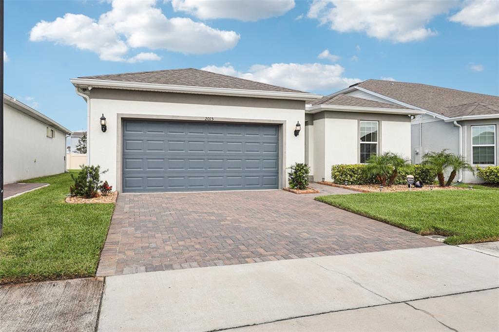 A single-story house with a gray garage door, paved driveway, and light-colored stucco exterior — 2015 SPRING SHOWER CIRCLE, KISSIMMEE, FL