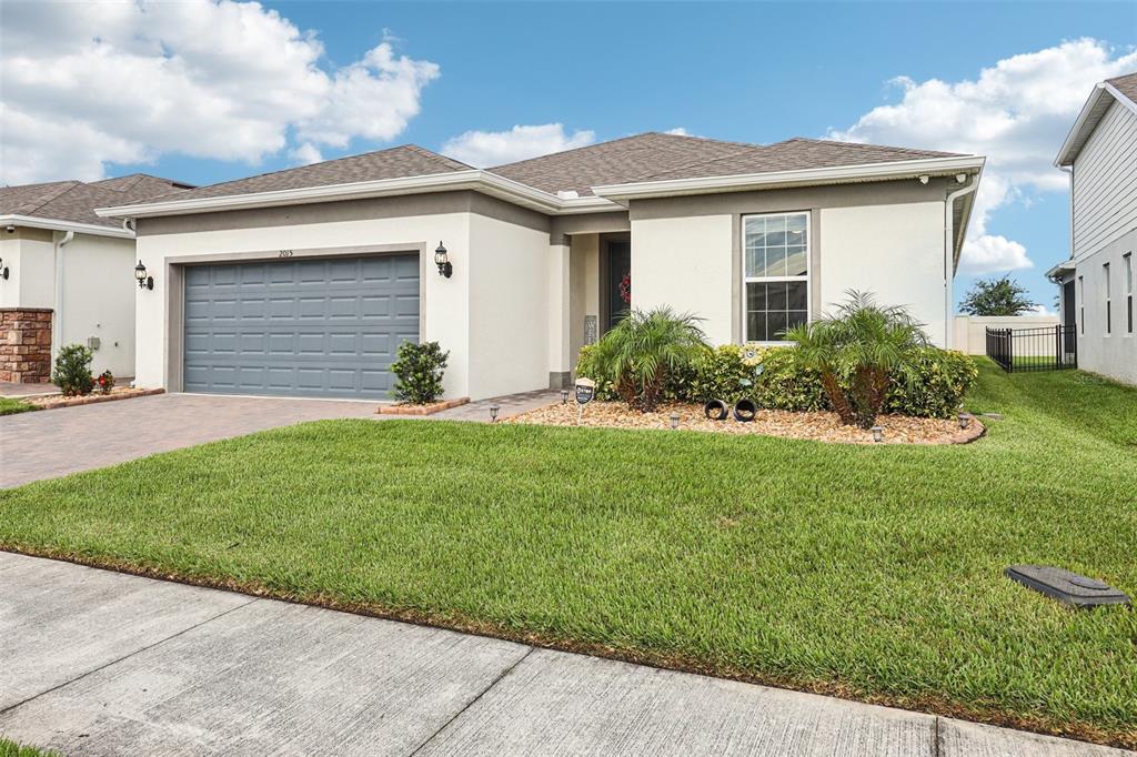 A single-story house with a gray garage door, stucco exterior, and a landscaped front yard — 2015 SPRING SHOWER CIRCLE, KISSIMMEE, FL
