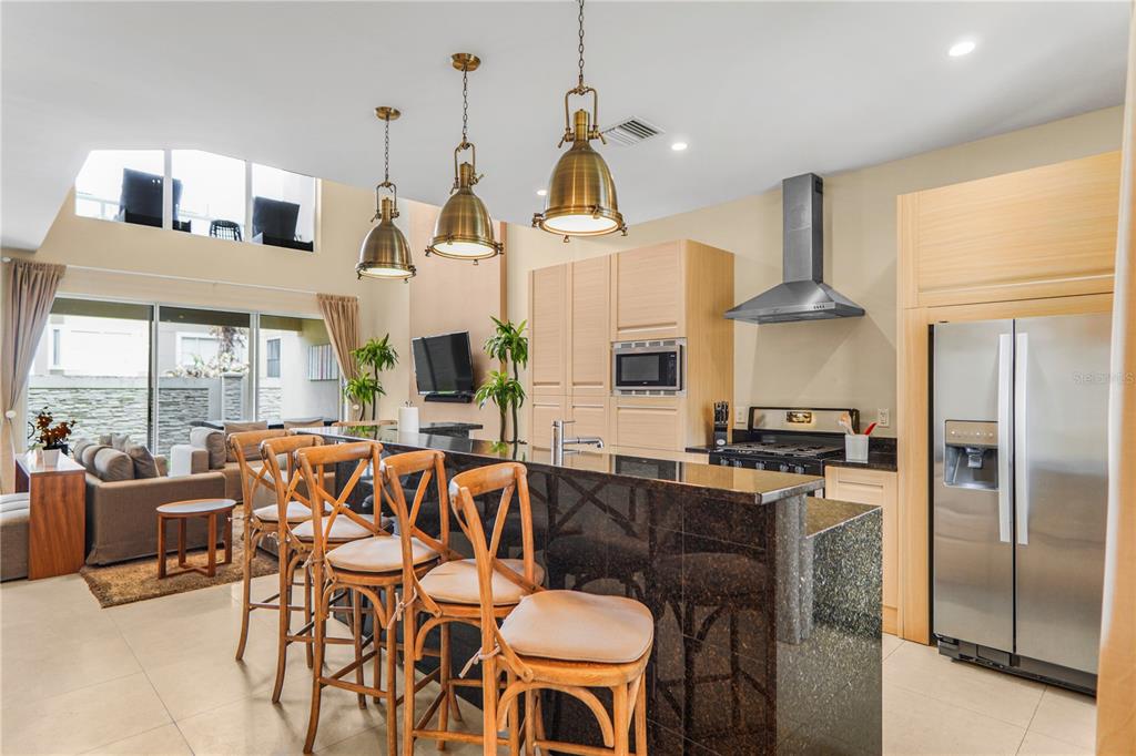 A kitchen with a dark granite island, wooden bar stools, and stainless steel appliances — 7605 RECIFE DRIVE, KISSIMMEE, FL