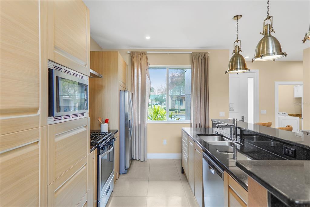 A kitchen features light wood cabinets, black granite countertops, stainless steel appliances, and pendant lighting — 7605 RECIFE DRIVE, KISSIMMEE, FL