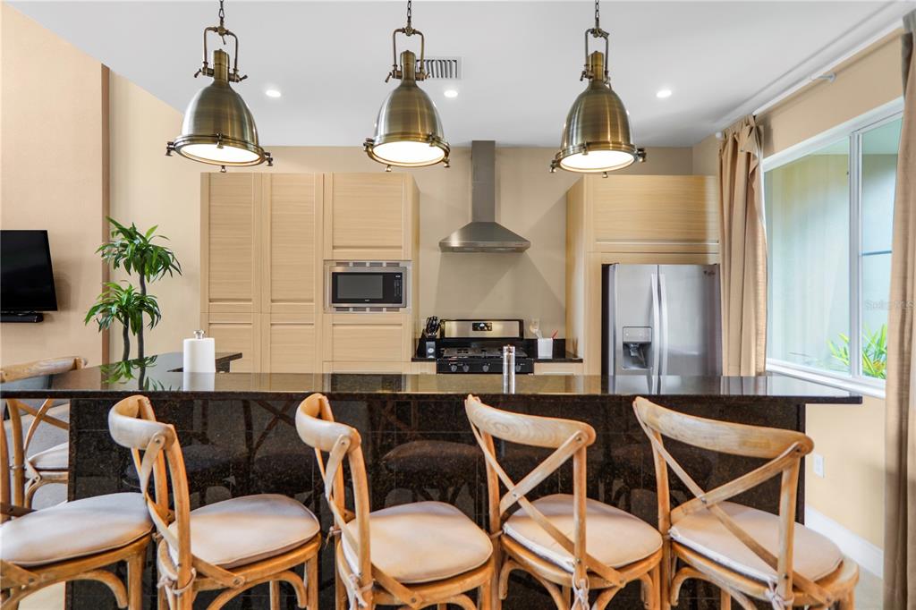 A kitchen features a dark granite island with four wooden chairs and stainless steel appliances — 7605 RECIFE DRIVE, KISSIMMEE, FL