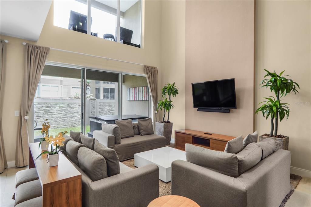 A living room features a high ceiling, large sliding glass doors, and a mounted television — 7605 RECIFE DRIVE, KISSIMMEE, FL