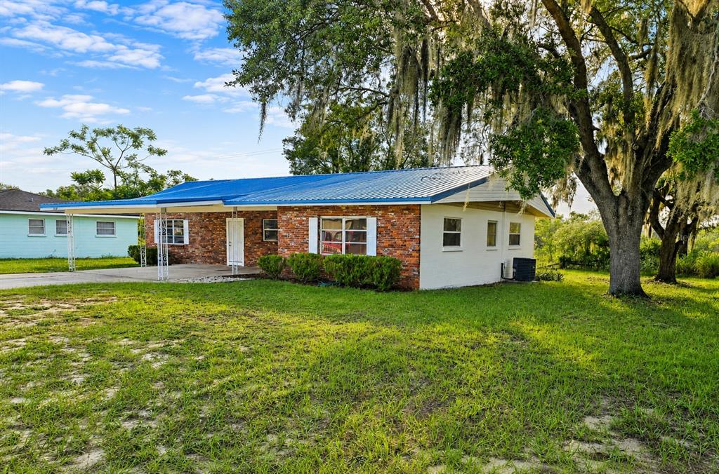 A single-story brick house with a blue metal roof and a large carport — 838 BLACKWOOD DRIVE, LAKE WALES, FL