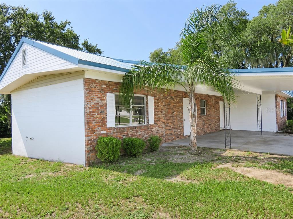A single-story brick house with a white-painted side wall, metal roof, and attached carport — 838 BLACKWOOD DRIVE, LAKE WALES, FL