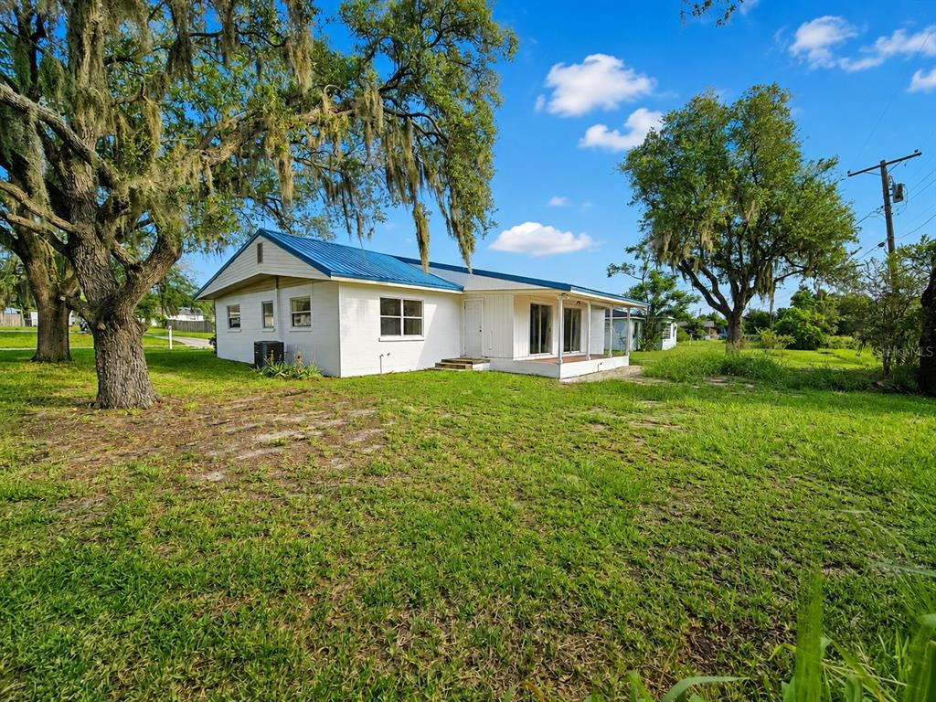 A white single-story house with a blue metal roof sits on a grassy lot — 838 BLACKWOOD DRIVE, LAKE WALES, FL