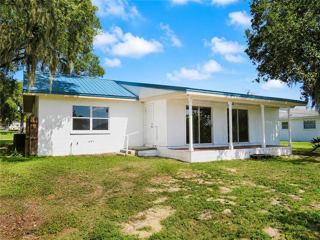 A white house with a blue metal roof and a covered porch sits on grass — 838 BLACKWOOD DRIVE, LAKE WALES, FL