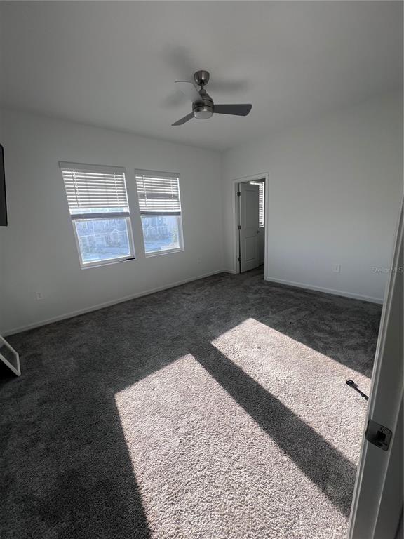 An empty bedroom features gray carpeting, white walls, two windows with blinds, and a ceiling fan — 2653 RUNNERS CIRCLE, CLERMONT, FL