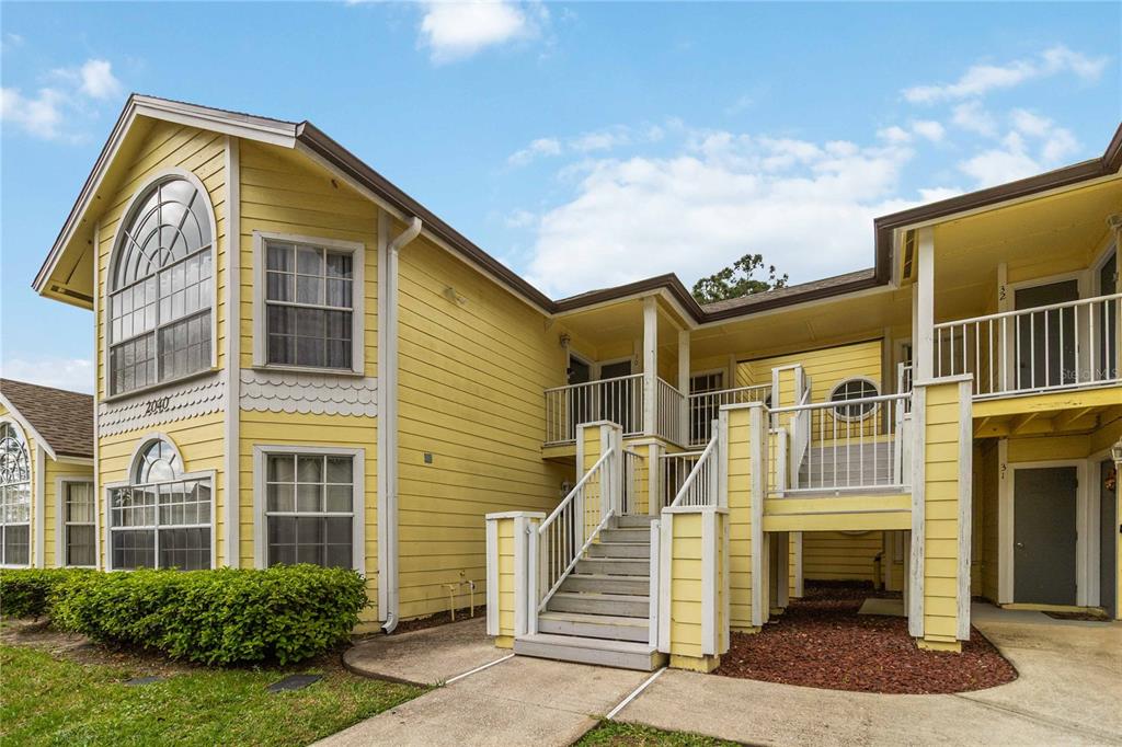 A two-story yellow apartment building features a central staircase leading to an elevated walkway — 2040 ROYAL BAY BOULEVARD UNIT 30, KISSIMMEE, FL
