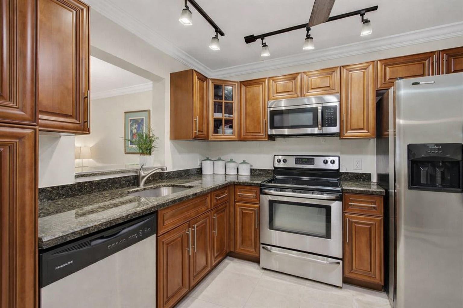 A kitchen with wood cabinets, granite countertops, stainless steel appliances, and track lighting — 19000 Stewart Circle # 4, Boca Raton FL 33496, BOCA RATON, FL