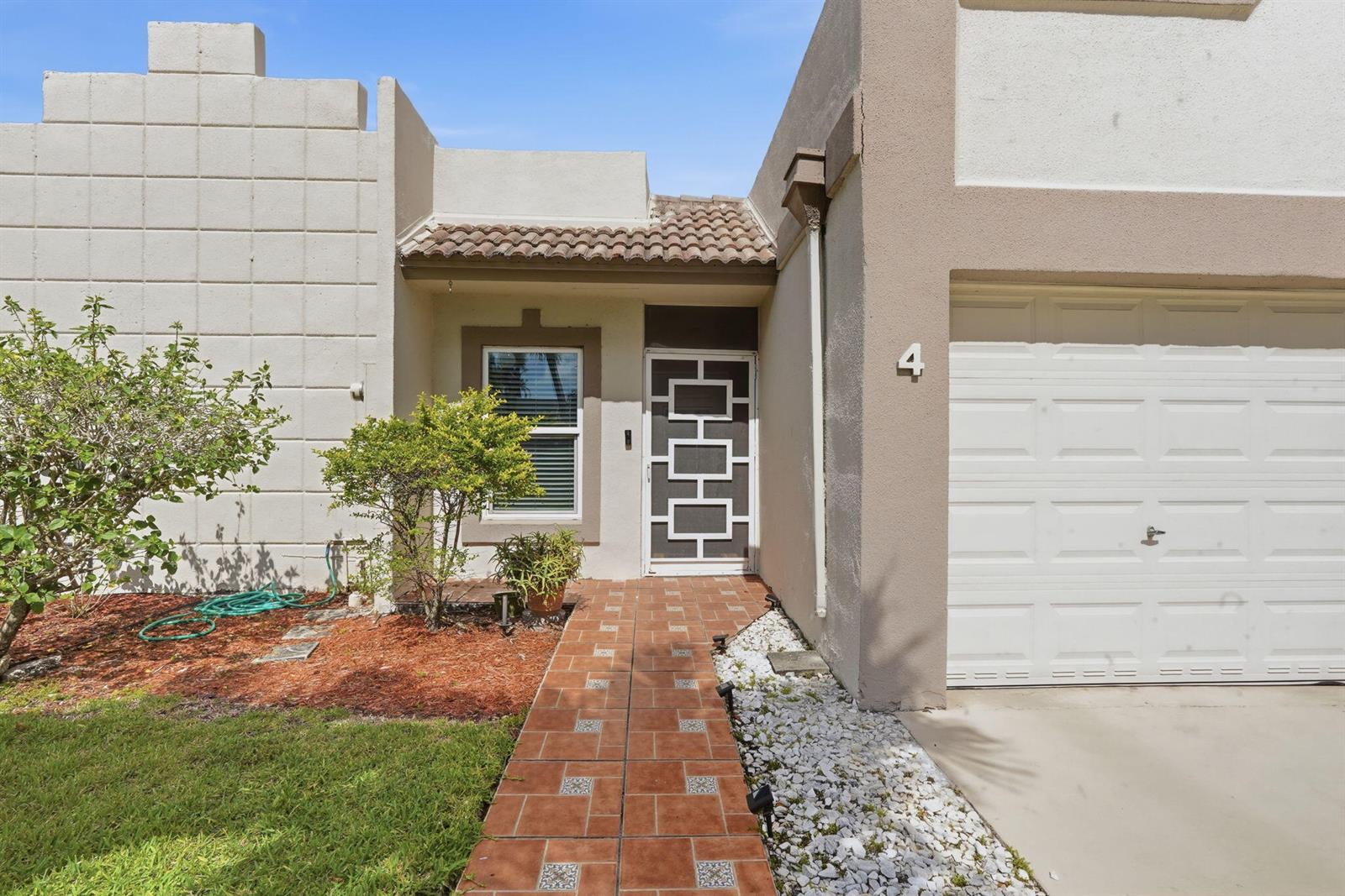 The exterior of a single-story home features a tiled walkway, a white garage, and landscaping — 19000 Stewart Circle # 4, Boca Raton FL 33496, BOCA RATON, FL