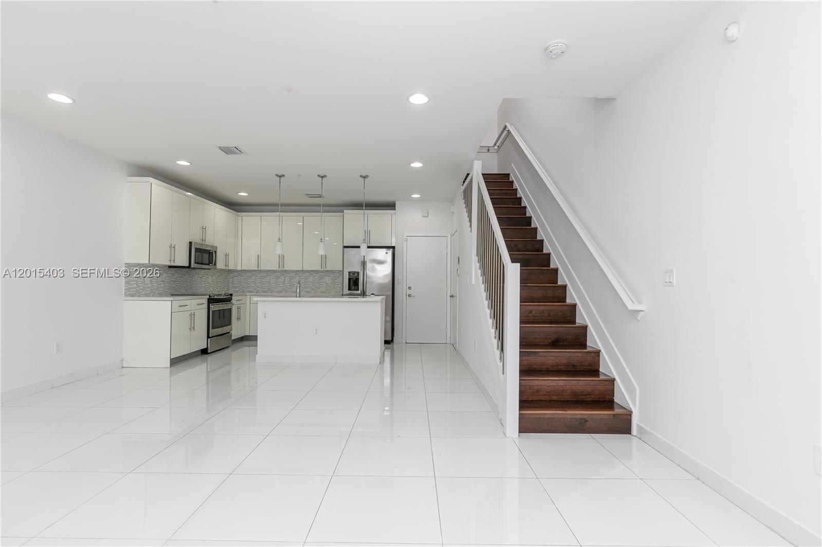 A modern kitchen features white cabinetry, stainless steel appliances, and an island with a sink — 2610 NE 213th St # 103, Miami FL 33180, MIAMI, FL