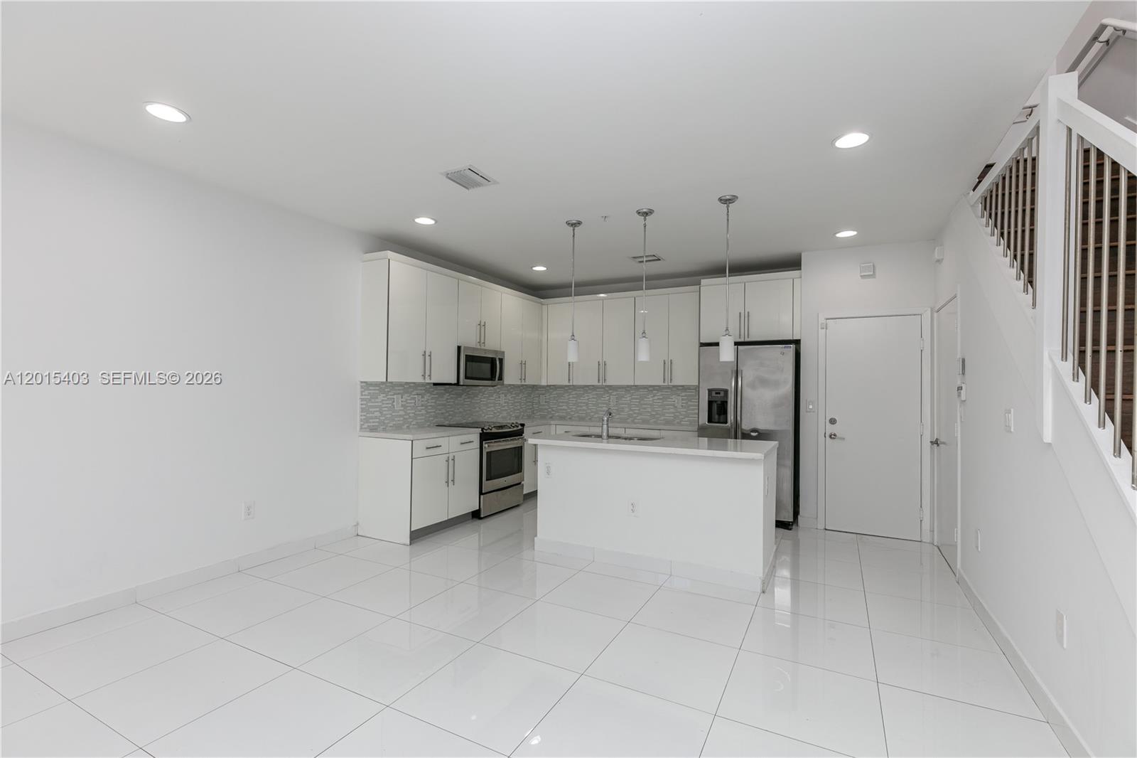 An empty room features white walls, light wood-look flooring, a window, and a sliding glass door — 2610 NE 213th St # 103, Miami FL 33180, MIAMI, FL