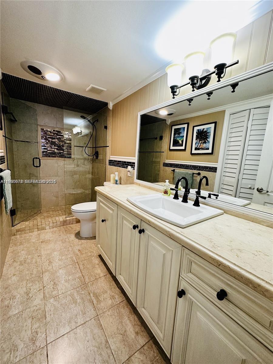 A bathroom features a stone countertop vanity, a glass-enclosed shower, and beige tile flooring — 1501 S Ocean Dr # 406, Hollywood FL 33019, HOLLYWOOD, FL