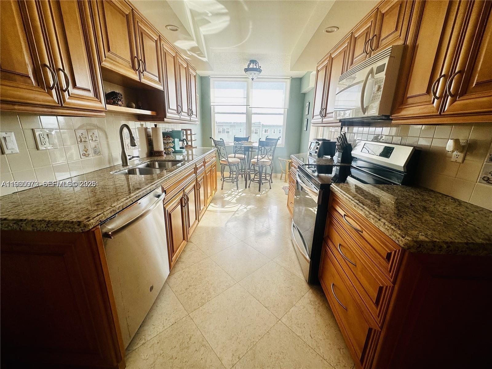 A galley kitchen features wood cabinets, granite countertops, stainless steel appliances, and a breakfast nook — 1501 S Ocean Dr # 406, Hollywood FL 33019, HOLLYWOOD, FL