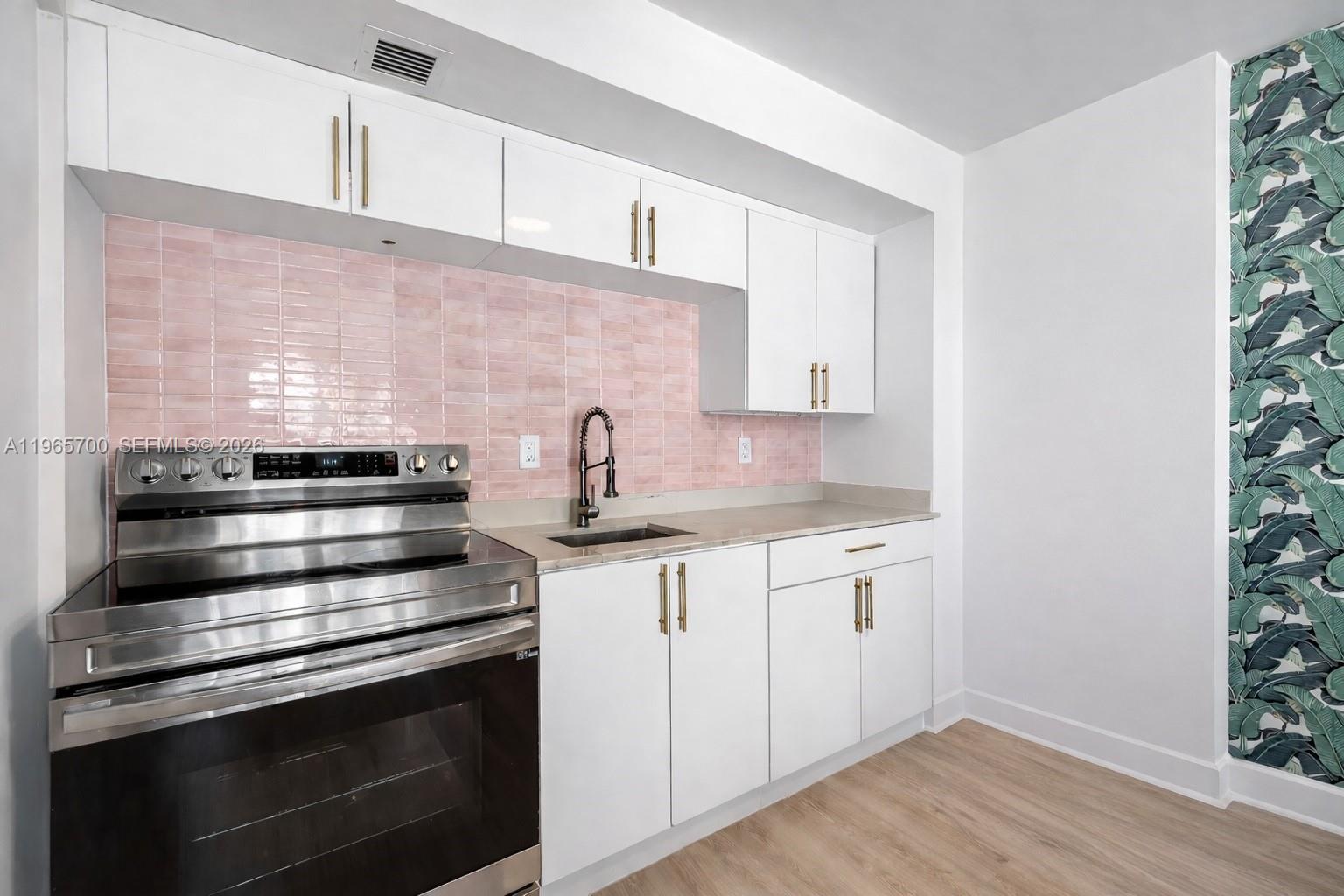 A kitchen features white cabinets, a pink tiled backsplash, stainless steel appliances, and wallpaper — 345 Ocean Dr # 718, Miami Beach FL 33139, MIAMI BEACH, FL