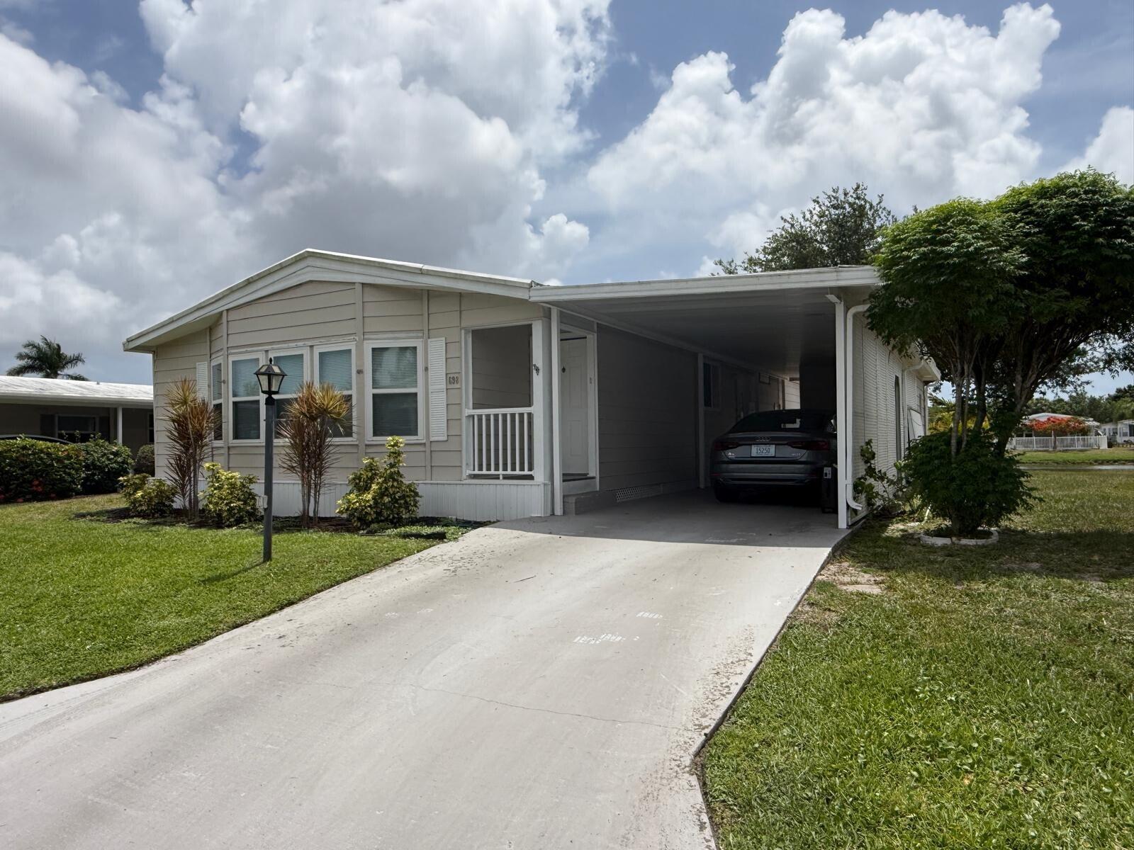 A beige manufactured home with a concrete driveway and a covered carport under a cloudy sky — 698 Sunny South Avenue, Boynton Beach FL 33436, BOYNTON BEACH, FL