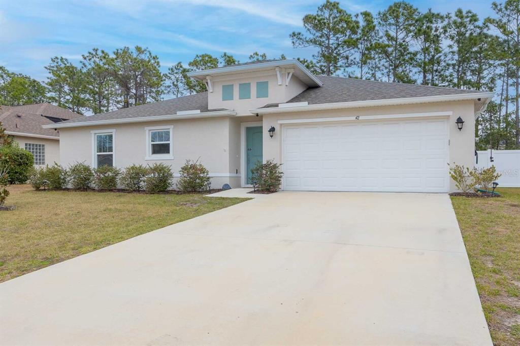 A single-story house with a beige stucco exterior, a two-car garage, and a blue door — 42 WOODBORN LANE, PALM COAST, FL